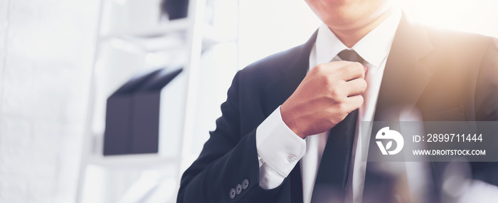 Businessman in black suit and adjusting necktie on office.