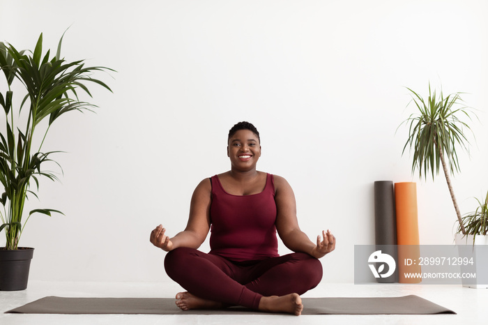 Happy plus size black woman doing yoga exercise at studio