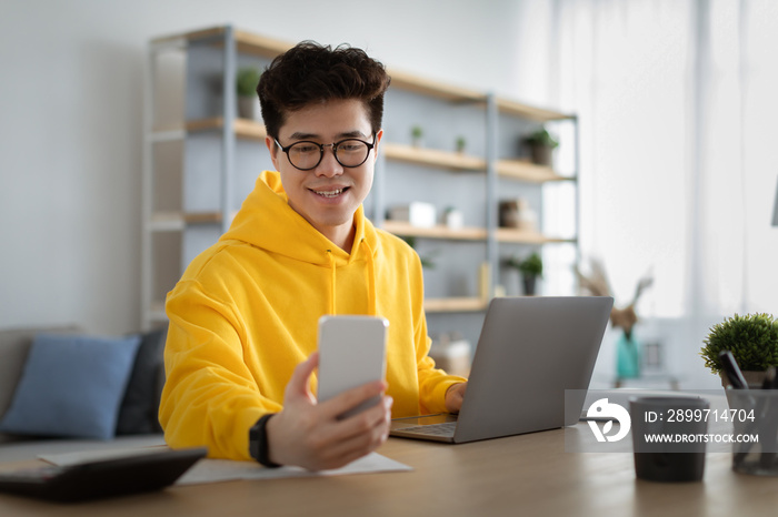 Asian man in glasses sitting at desk using cell phone