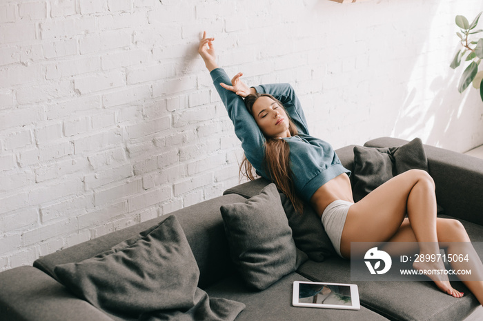 attractive woman stretching on sofa with digital tablet