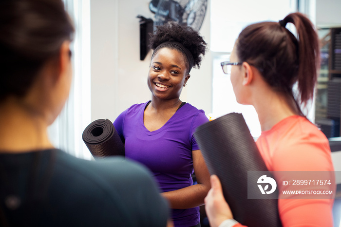 Smiling female athletes with exercise mats talking while standing in class