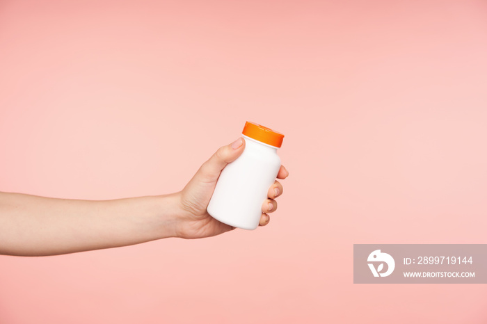 Studio photo of young females hand with nude manicure keeping bottle with pills in it while being i