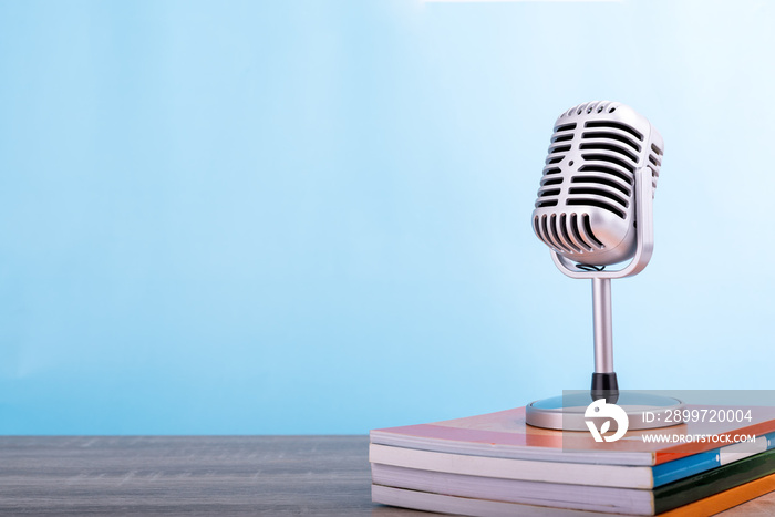 Education teaching concept : Retro microphone with many book put on wooden table isolated on blue ba