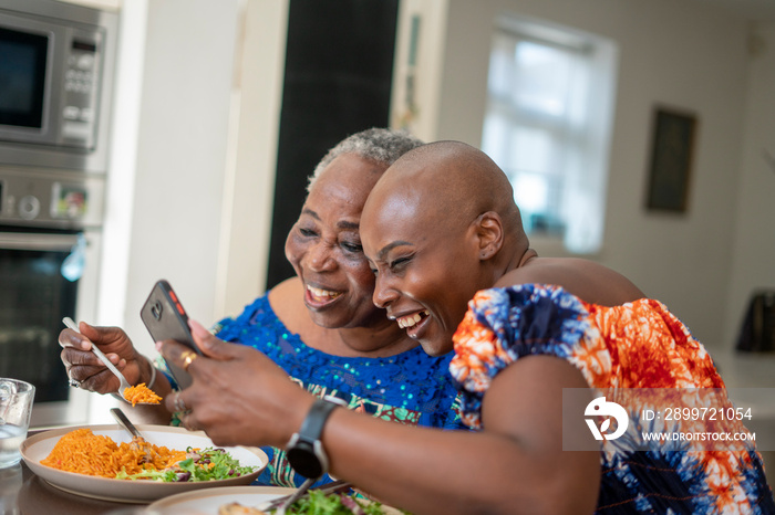 微笑的女人和成年女儿一起吃晚饭，看着智能手机