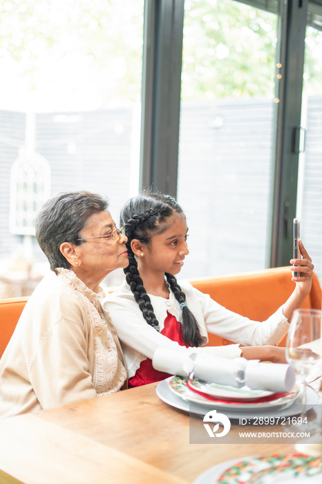 Smiling girl with grandmother taking?selfie?at table