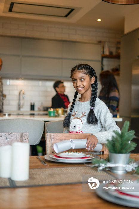 Girl placing Christmas cracker on table, mother and grandmother in background