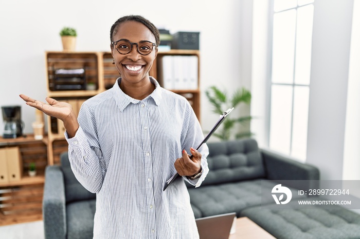 African woman working at psychology clinic smiling cheerful presenting and pointing with palm of han