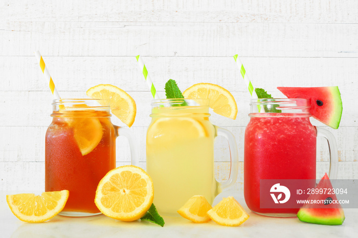 Variety of summer drinks in mason jar glasses with fruit against a white wood background. Iced tea, 