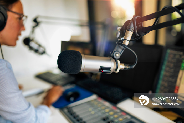 Microphone in a podcasting studio, host and the broadcasting equipment in the background