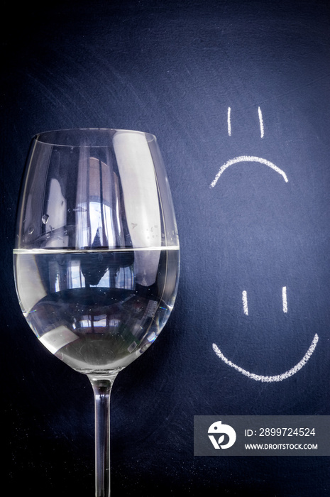 Half-full or half-empty glass of water, with an happy smiley and unhappy smiley, showing optimism or