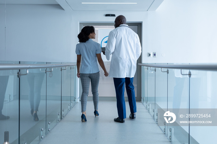 Rear view of diverse male and female doctor walking in hospital corridor and talking