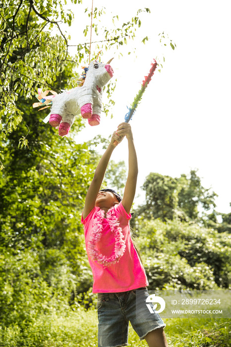 Boy (8-9) in pink t-shirt and garland playing with toy horse hanging on tree