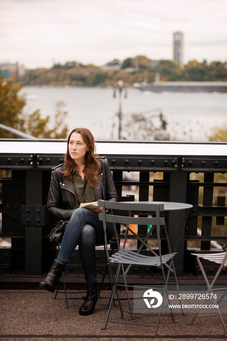 Young woman sitting outdoors at table with book