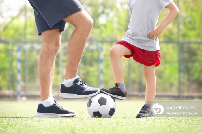 Legs of father and son with ball on soccer pitch