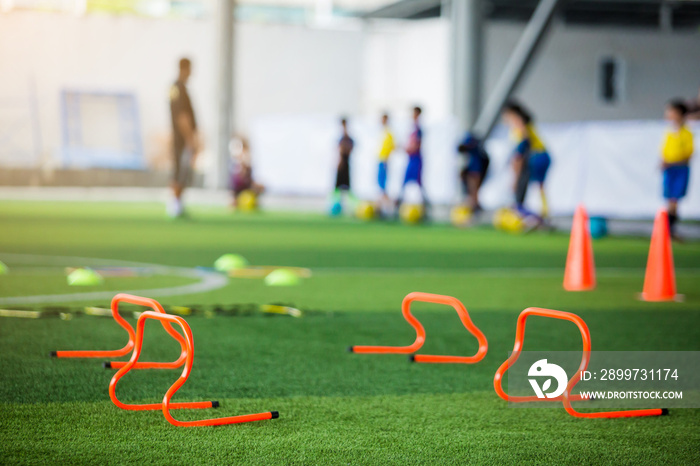 orange hurdles on green artificial turf with blurry coach and kid soccer are training.