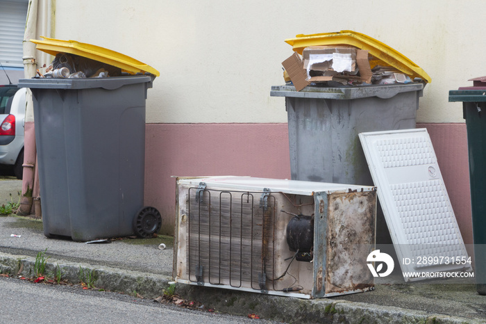 Full garbage bin and left-behind fridge in a street in Brest