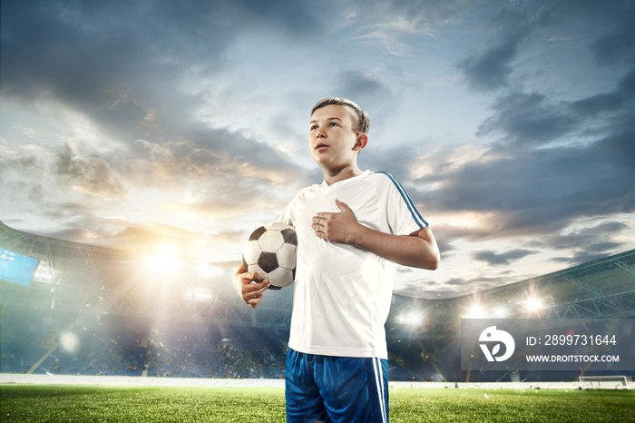 体育场里拿着足球的小男孩。天空背景下的足球运动员获胜