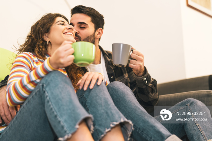 Young couple drinking coffee cup sitting on floor next sofa - Happy lovers having tender moments tog