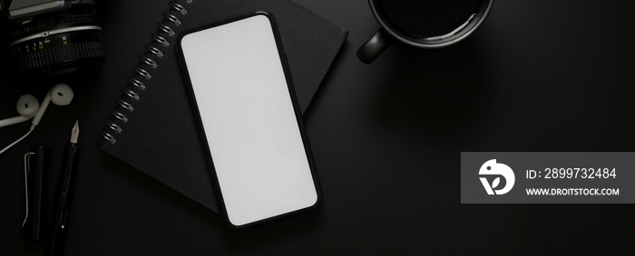 Blank screen smartphone above black notebook and coffee cup on dark modern worktable