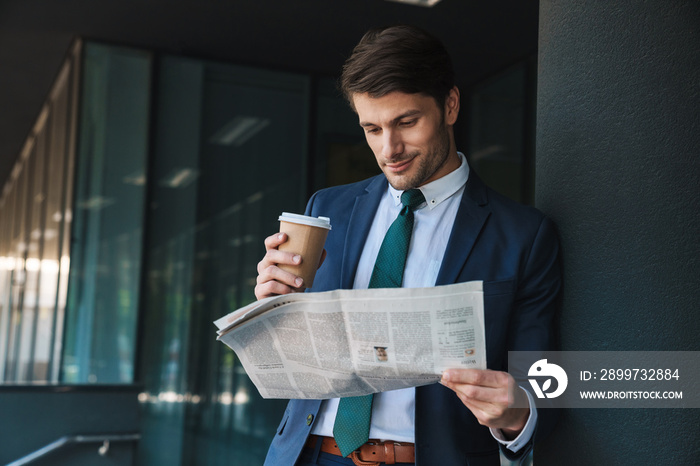 Photo of successful businessman reading newspaper and drinking coffee while standing outside job cen