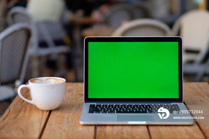 close up one green screen laptop computer on wooden table with a cup of coffee. blur sidewalk cafe b