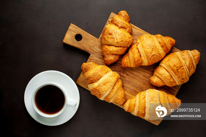 coffee and croissants on wooden cutting board, on the background concrete