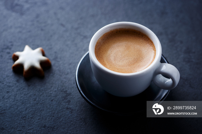 Cup of coffee and Christmas cookie (cinnamon stars) on dark stone background. Close up.