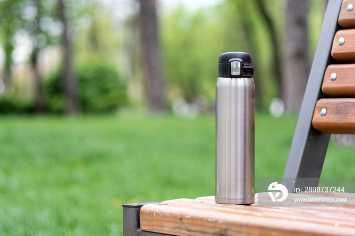 Steel thermal mug standing on a park bench. Thermos on a bench in the park.