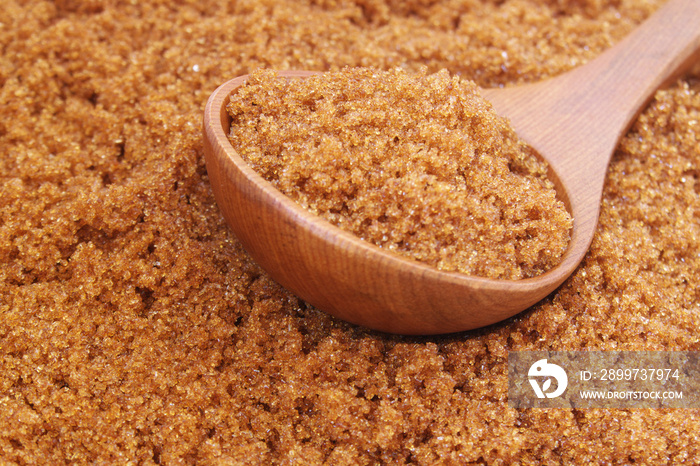 Dark brown sugar and wooden spoon  on sugar background