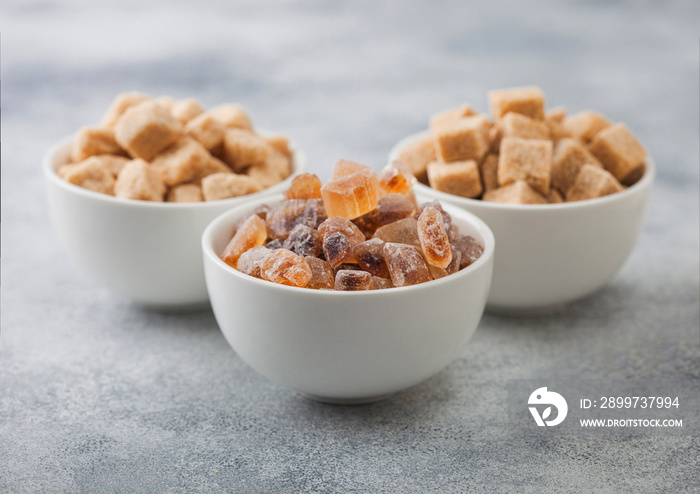 White ceramic bowl plates of natural brown unrefined and caramelized sugar cubes on light table back