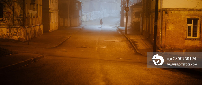 Lonely woman walking in foggy old city with street lights in a coat