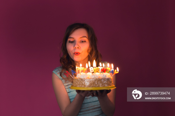 派对上漂亮女孩拿着生日蛋糕吹蜡烛的肖像