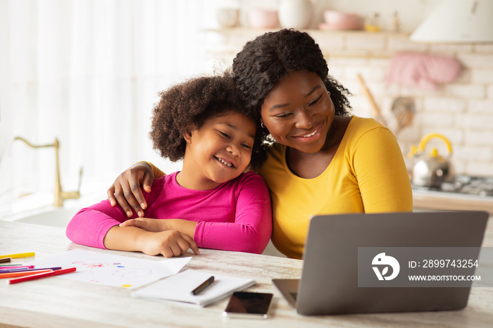 Happy African American Mom And Her Little Daughter Using Laptop In Kitchen