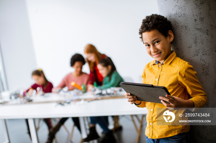 Cute little boy standing in front of kids programming electric toys and robots at robotics classroom