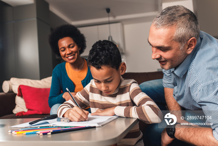 Parents helping their son with his homework at home in living room.