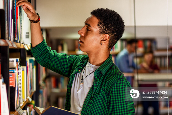 Young male student study in the library searching new book on bookshelf.