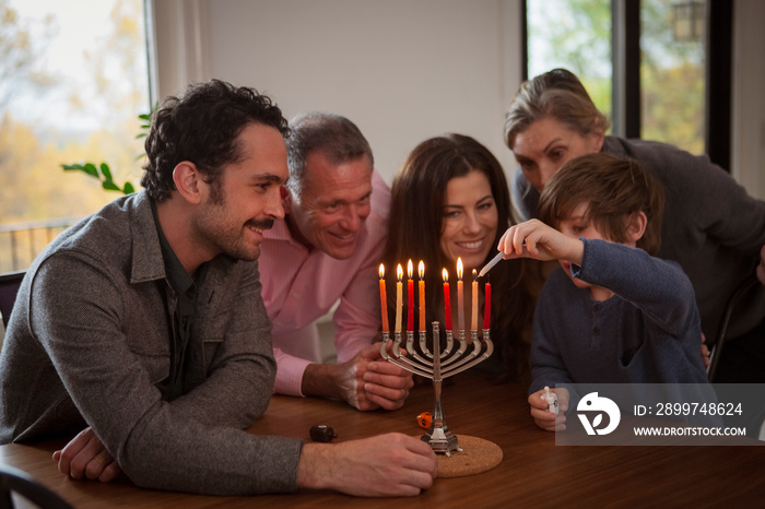 Happy family assisting boy in burning candles on menorah during Hanukkah festival at home