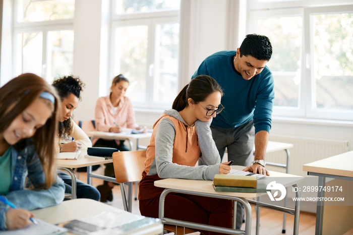 Female high school student learns with teachers help in classroom.