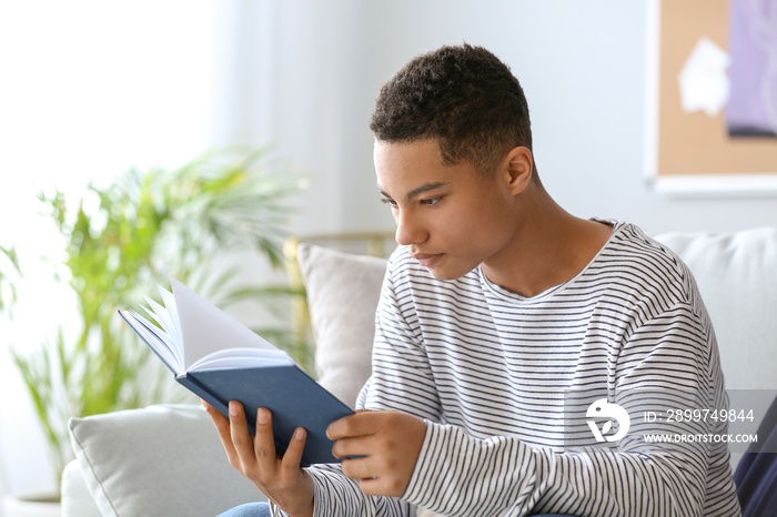 African-American teenage boy reading book at home