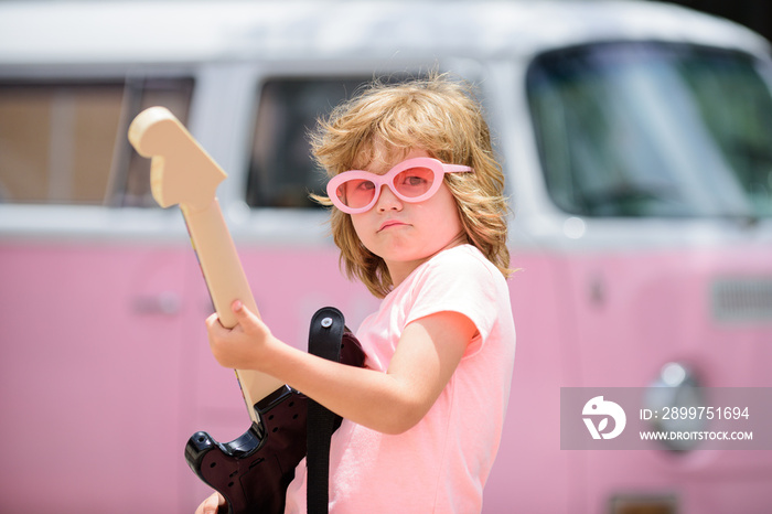 Musician child with a guitar. Joyful cute kid improvising. Happy kid enjoys music over colorful pink