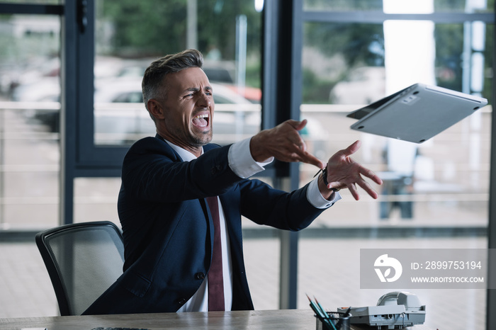 angry businessman throwing in air laptop in office