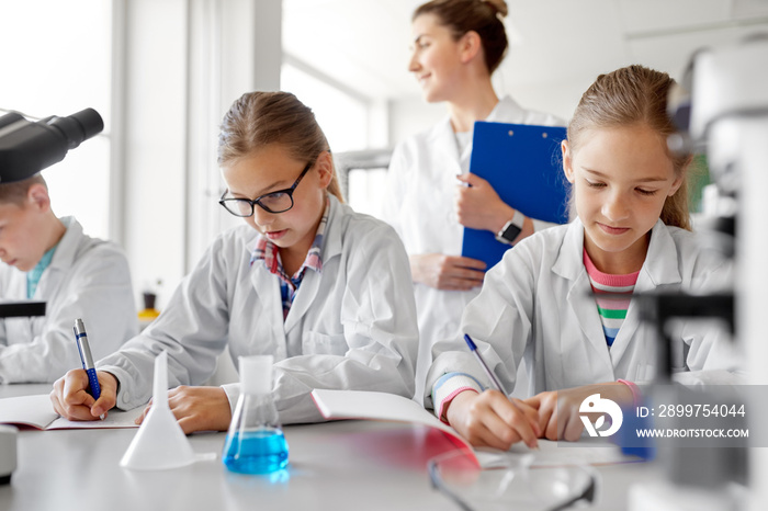 education, science and children concept - teacher and students studying chemistry at school laborato