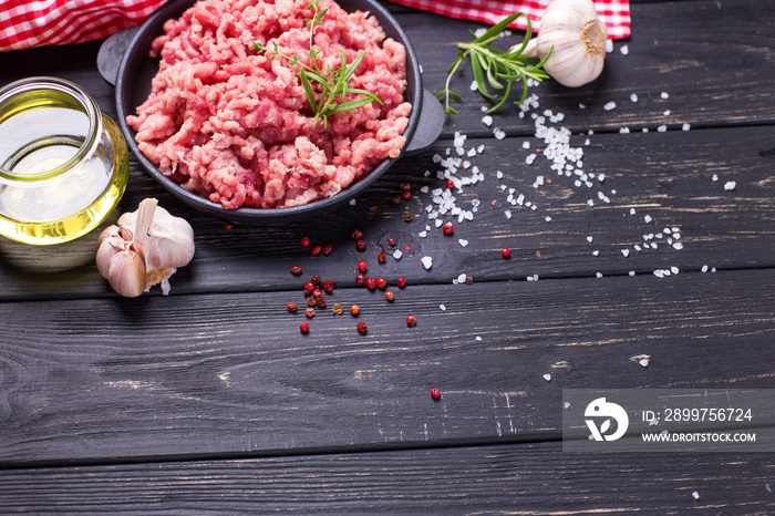 Raw minced meat in bowl  with ingredients for cooking on  black table.