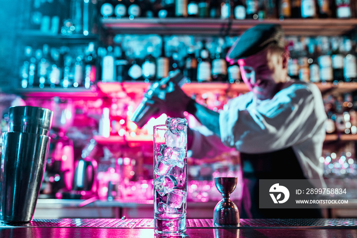 Expert barman is making cocktail at night club or bar. Glass of fiery cocktail on the bar counter ag