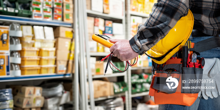 Electrician holds multimeter tester in hand, helmet with protective goggles. Construction industry, 