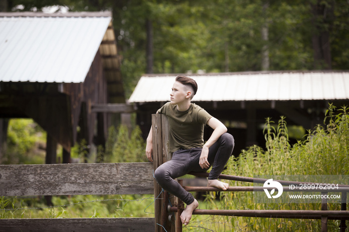 Teenage boy sitting on gate against cabins