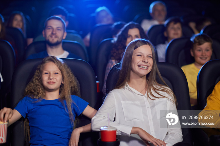 Young laughing girl with younger sister in cinema.