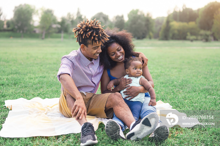 Happy black family doing a picnic outdoor - Mother and father having fun with their daughter in a pa