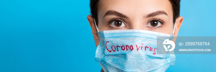 Portrait of pretty woman wearing medical mask with coronavirus text at blue background. Coronavirus 