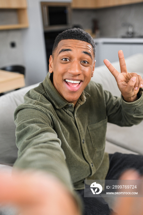 Great selfie. Multiracial young guy gesturing to the smartphone camera, while making funny photos at